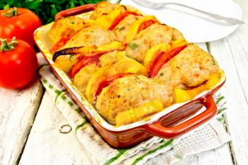 Cutlets of turkey meat baked with red tomatoes and yellow pepper in a ceramic roasting pan on a kitchen towel, parsley on a wooden boards background