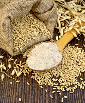 Flour oat in a wooden spoon, a bag of oat stalks of oats on the background of wooden boards