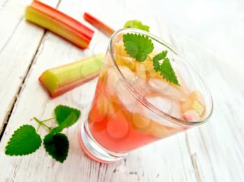 Lemonade with rhubarb and mint in a glass, the stems and leaves of rhubarb on a wooden boards background