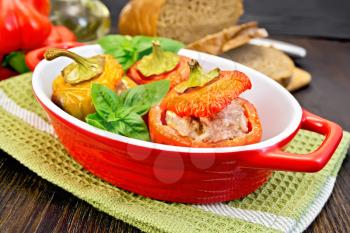 Three sweet peppers stuffed with meat and rice with basil leaves in red roasting pan on a green napkin, bread on a dark wooden board
