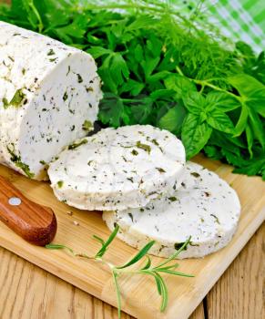 Homemade cheese with herbs and spices, cut into slices, knife, parsley, rosemary and basil, napkin on a background of wooden boards