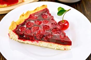 Piece of sweet pie with cherry berries and jelly in a plate with a fork on a dark wooden board