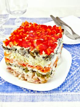 Layered salad with chicken, egg, mushrooms and cucumber, carrots and peppers, seasoned mayonnaise on a background of a blue tablecloth