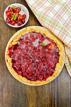 Sweet pie with cherries and jelly, napkin, plate of cherries on a background of the wooden planks on top