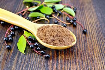 Flour of bird-cherry in a spoon with berries and green leaves on a background of dark wooden boards