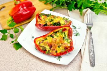Sweet pepper stuffed with sausage, egg and cheese with dill in white plate, napkin, fork and parsley on table background