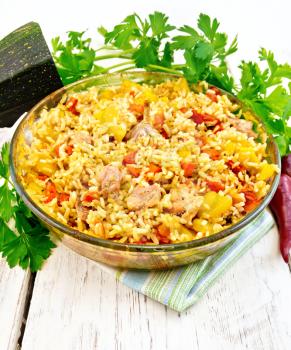 Rice with chicken, tomatoes, carrots, zucchini and garlic in a glass pan on a napkin, parsley on the background light wooden boards