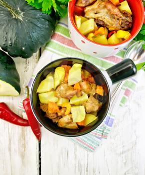 Roast with chicken, potatoes, squash and peppers in two portioned white pot on a napkin, spoon, parsley on a background of wooden boards on top