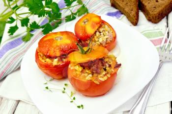 Tomatoes stuffed with meat and steamed wheat bulgur, a sprig of thyme in a plate, napkin, fork, bread and parsley on a wooden board background