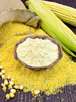 Flour corn in a clay bowl, grits, cobs and grains, a bag on a wooden boards background