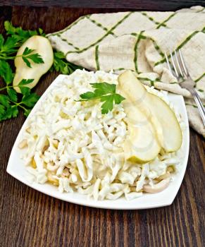 Salad of squid, rice, pears and eggs in a plate, parsley, slice fruit, napkin and fork on the background of wooden boards