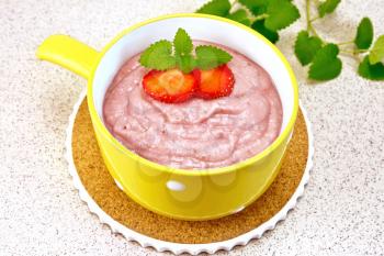 Strawberry soup with berries and mint in a yellow bowl on stand, towel on a background of a granite table