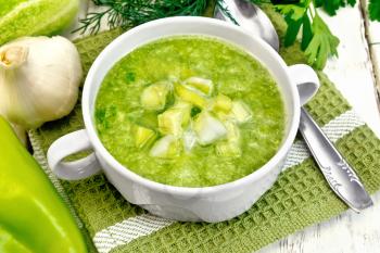 Cucumber soup with green peppers and garlic in a bowl on green napkin, parsley on the background light wooden boards