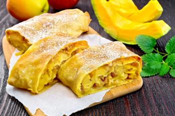 Strudel pumpkin and apple with raisins on paper, mint, fruit and vegetables on the background of wooden boards