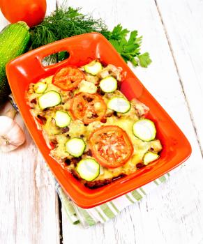 Baked minced meat, tomatoes and zucchini in a brazier on a napkin on a wooden board background