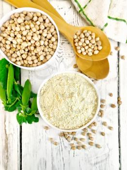 Flour chickpeas and chick-pea in white bowls and spoons, pods of green beans on the background of the wooden planks on top