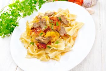 Macaroni Farfalle with turkey meat, tomato, yellow sweet pepper with sauce in a plate, garlic, parsley on a light wooden board background