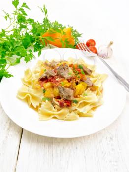 Macaroni Farfalle with turkey meat, tomato, yellow sweet pepper with sauce in a plate, garlic, parsley and fork on a wooden plank background
