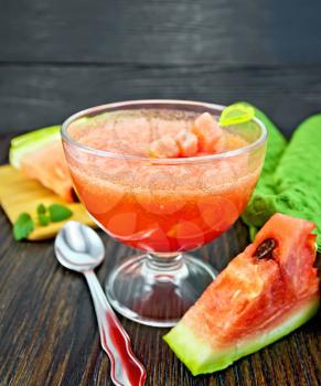 Jelly airy watermelon in a glass bowl, spoon, towel on a wooden plank background