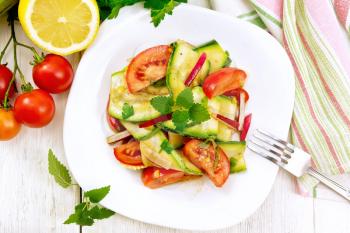 Salad of young zucchini, radish, tomato and mint, seasoned with lemon juice and soy sauce in a plate, napkin on a wooden board background from above