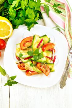 Salad of young zucchini, radish, tomato and mint, flavored with lemon juice and soy sauce in a plate, napkin on a light wooden board on top