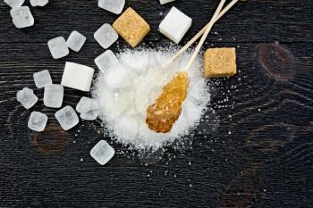 Sugar white and brown granular, crystalline and cubes on the background of a black wooden board from above