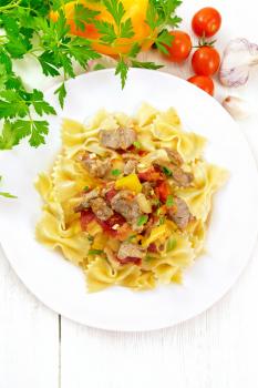 Macaroni Farfalle with turkey meat, tomato, yellow sweet pepper with sauce in a plate on the background of a light wooden board on top