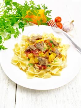 Macaroni Farfalle with turkey meat, tomato, yellow sweet pepper with sauce in a plate, garlic, parsley and fork on a light wooden board background