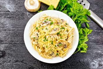 Fusilli pasta with champignons in creamy sauce, parsley and grated cheese in a plate on background of black wooden board from above