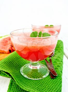 Jelly airy watermelon with mint in two glass bowls, a spoon on a green towel against a light wooden board