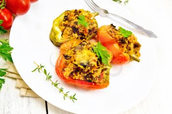 Pepper sweet, stuffed with mushrooms, tomatoes, couscous and cheese in a white plate on kitchen towel, fork, parsley against the background of light wooden board