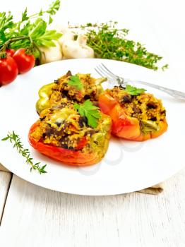 Pepper sweet, stuffed with mushrooms, tomatoes, couscous and cheese in a white plate on towel, fork, parsley against the background of light wooden board