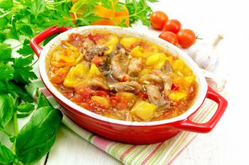 Ragout of turkey meat, tomato, yellow sweet pepper and onion with sauce in a red brazier on a napkin on a wooden board background