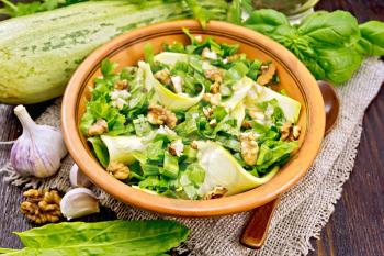 Salad of young zucchini, sorrel, garlic and nuts, seasoned with vegetable oil in a plate on napkin of sackcloth on a background of a dark wooden board
