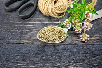 Thyme dry in a metal spoon, a bunch of fresh herbs with pink flowers, a skein of twine and scissors on the background of a wooden board