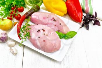 Chicken breast with hot pepper and thyme in a white plate, napkin, parsley and basil, onion, garlic and vegetables on a wooden plank background