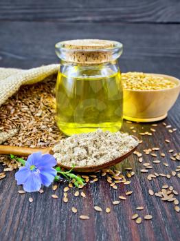 Flaxseed flour in a spoon, oil in a glass jar, flax flower, brown seeds in a bag and white linen seeds in a bowl on a wooden board background