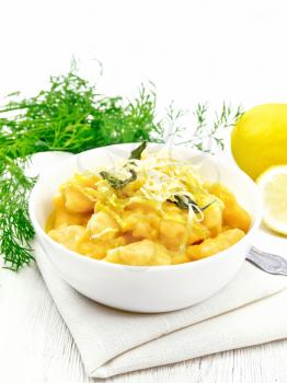 Pumpkin gnocchi with sage, lemon, cheese and butter in a bowl, a towel against the background of light wooden board