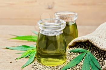 Hemp oil in two glass jars, grain in the bag and on the table, cannabis leaves on the background of the old board