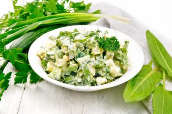 Salad of cucumber, sorrel, boiled potatoes, eggs and herbs, dressed with mayonnaise in white plate, parsley, green onions and napkin on wooden board background