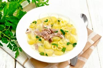 Chicken meat soup, pasta with cream and cilantro in a plate on a towel, parsley, metal spoon on a wooden board background