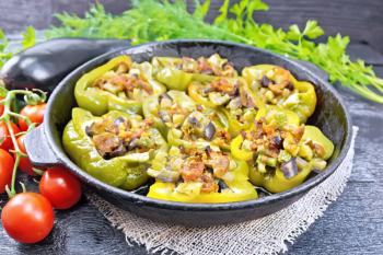 Pepper sweet stuffed with mushrooms, tomatoes, zucchini, eggplant and onions, seasoned with wine, garlic, thyme and spices in a pan on a napkin of burlap on black wooden board background