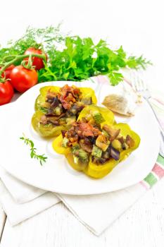 Sweet pepper stuffed with mushrooms, tomatoes, zucchini, eggplant and onions, seasoned with wine, garlic, thyme and spices in a white plate on a kitchen towel against the background of light wooden board