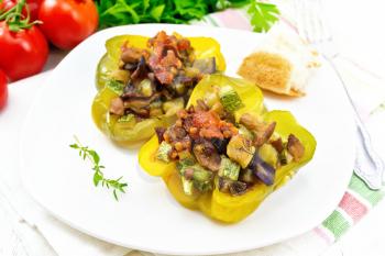 Pepper sweet stuffed with mushrooms, tomatoes, zucchini, eggplant and onions, seasoned with wine, garlic, thyme and spices in a white plate on kitchen towel against white wooden board