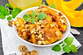 Pumpkin with walnuts and honey in a bowl on a towel, mint and fork on a background of dark wooden boards