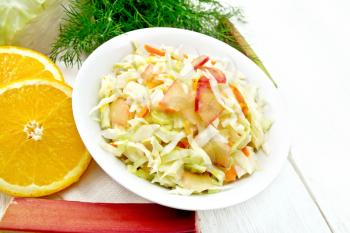 Fresh cabbage, carrot and rhubarb salad with orange juice, honey and mayonnaise dressing in a plate on a napkin, dill and fork on white wooden board background