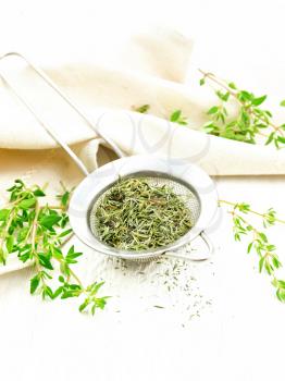 Thyme dry in a metal strainer, fresh greens of grass and linen towel on the background of light wooden boards