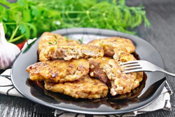 Fritters of minced meat in a plate with a fork on napkin, garlic, parsley and hot pepper on wooden board background