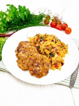 Fritters of minced meat with stewed cabbage in a plate, fork on kitchen towel, tomatoes, parsley and chard on wooden board background
