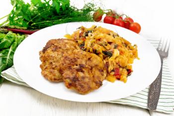 Fritters of minced meat with stewed cabbage in a plate, fork on a towel, tomatoes, parsley and chard on wooden board background